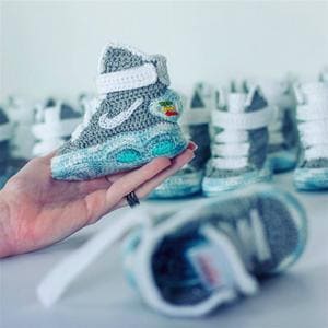 Main tient une minuscule sneaker tricotée devant d'autres.