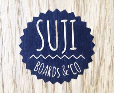 Logo de 'SUJI Boards & Co' sur fond en bois