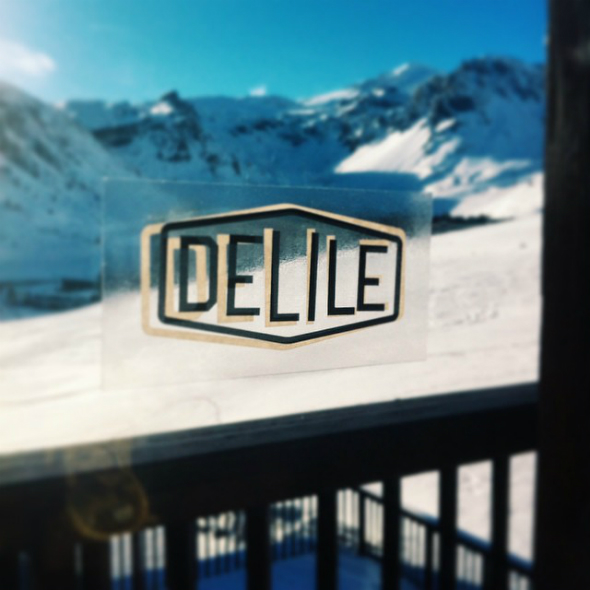 Sticker personnalisé DELILE en sérigraphie noir et blanc apposé sur une vitre avec paysage enneigé en arrière-plan