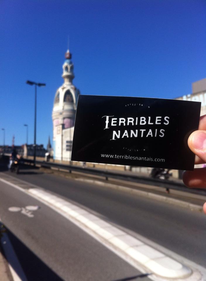 Autocollant personnalisé 'Terribles Nantais' tenu à la main avec un bâtiment flou en arrière-plan