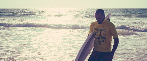 Surfeur tenant sa planche sur la plage au coucher de soleil