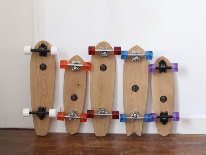 Cinq skateboards en bois avec des roues colorées, alignés sur un mur 