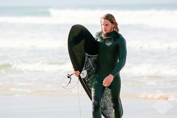 Surfeur tenant sa planche de surf sur une plage avec la mer en arrière plan