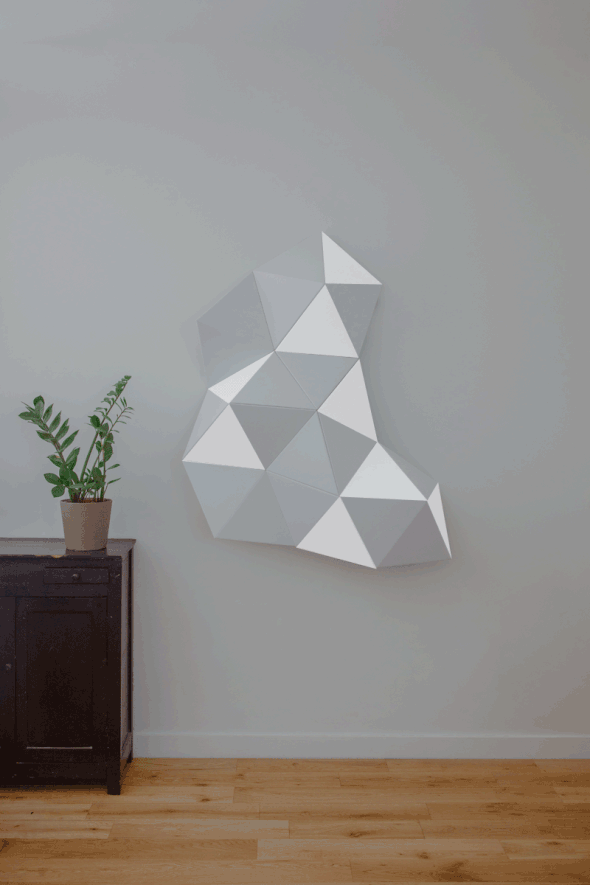 Sticker mural en forme géométrique 3D personnalisé accroché sur un mur intérieur à côté d'une plante