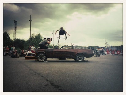 Skateboarder effectuant une figure au-dessus d'une voiture vintage lors d'une compétition de skate en extérieur