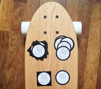 stickers personnalisés avec logo Suji posés sur une planche de skateboard en bois