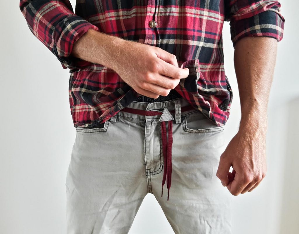 Personne ajustant sa chemise à carreaux de marque Waph devant un fond uni